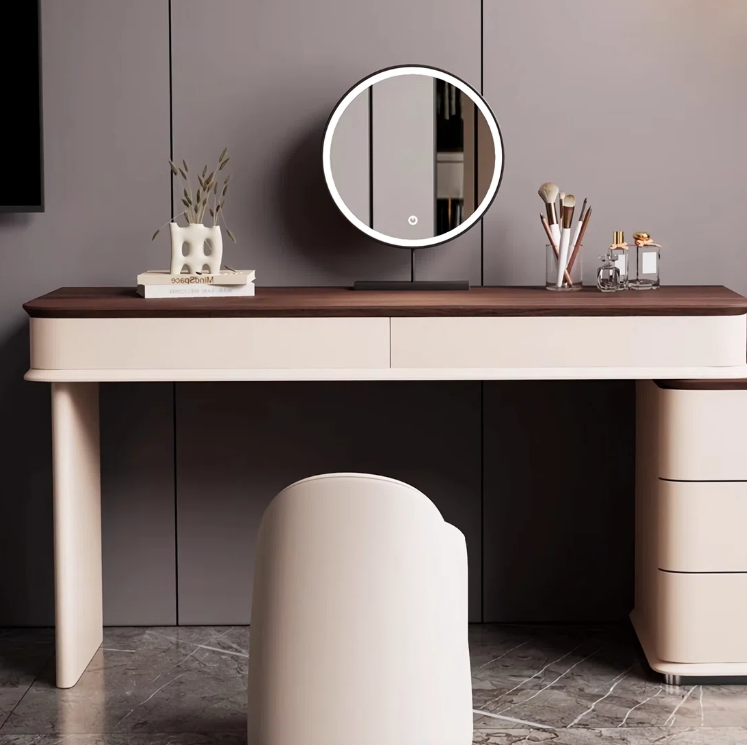 Modern dressing table with round mirror, stool, and various items against a gray wall.