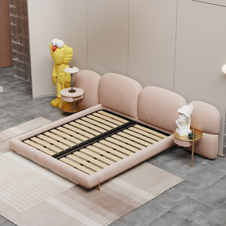 Pink upholstered bed with wooden slats in a room setting.