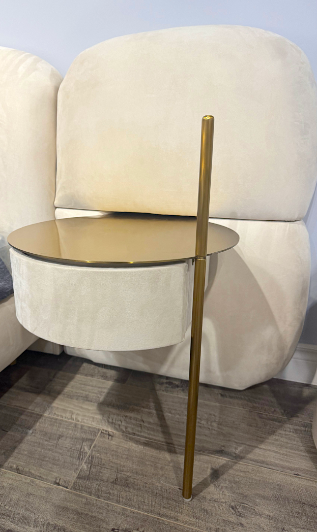 Beige armchair with a small round table and gold leg on a wooden floor.