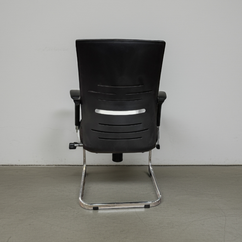 Black office chair with chrome legs on a gray floor and white wall