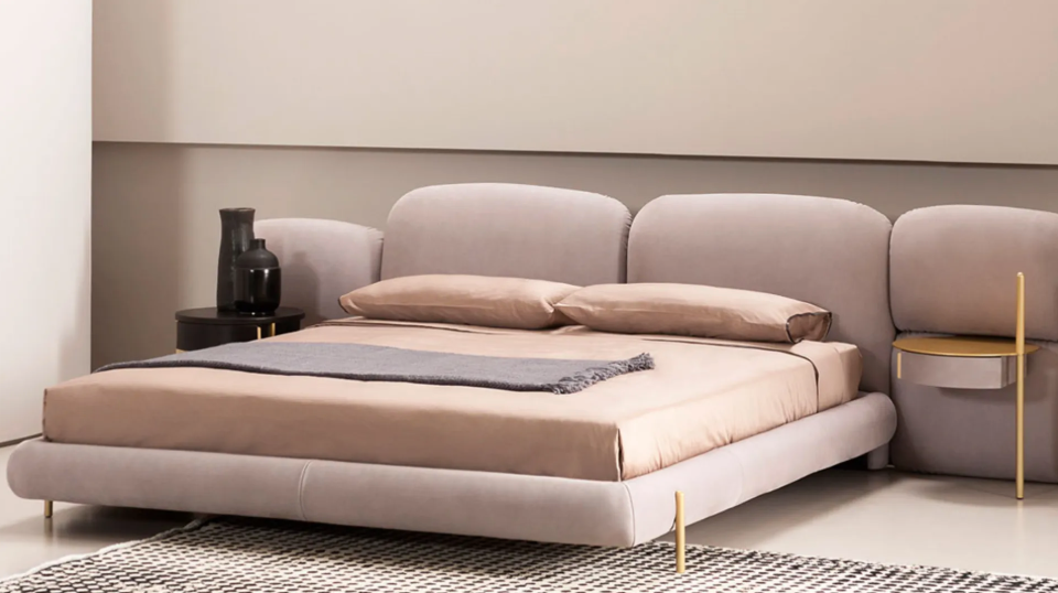 Modern bed with beige bedding and pillows in a minimalistic room.