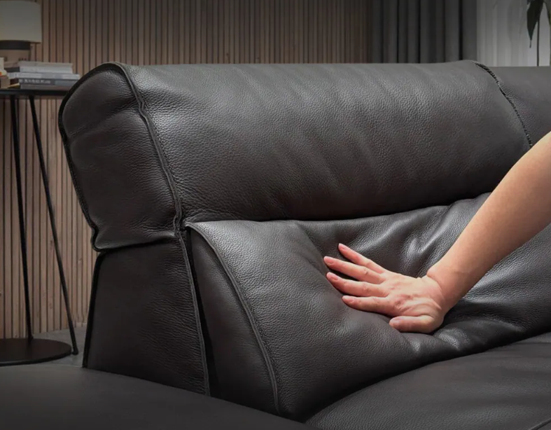 Person's hand touching a black leather sofa in a room with a lamp and books on a table genesis furniture