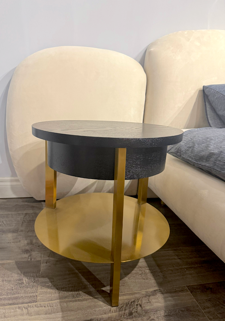 Round side table with gold legs and black top in a room setting.