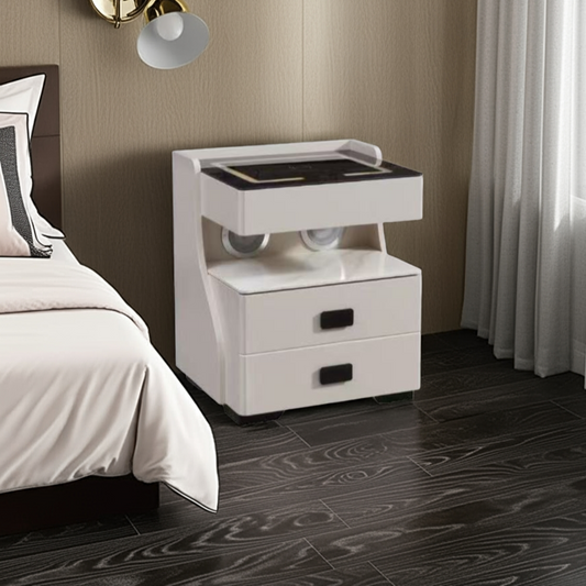 White nightstand with black top next to a bed in a bedroom setting.